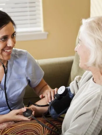 Nurse taking senior woman’s blood pressure nurse at home